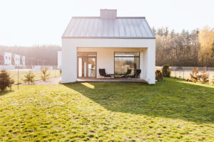 Modern house with terrace and garden furniture overlooking a large green lawn surrounded by a forested area