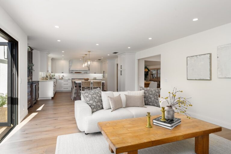 Open-concept living room and kitchen with white cabinets, wooden flooring, and cozy furniture