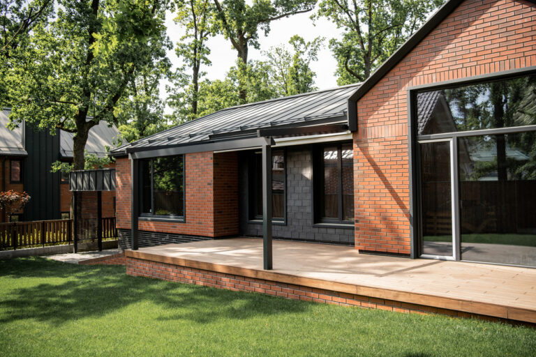 Modern brick home with large windows and a wooden deck surrounded by greenery