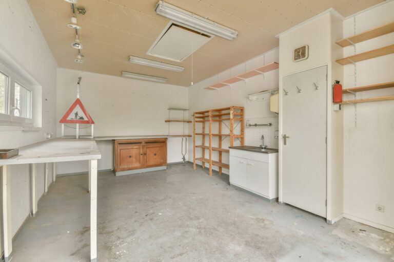 Empty garage with shelves, workbench, and sink, ready for conversion