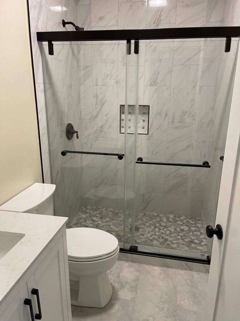 Modern ADU bathroom in San Diego featuring glass shower enclosure, marble-look tile, and sleek white vanity