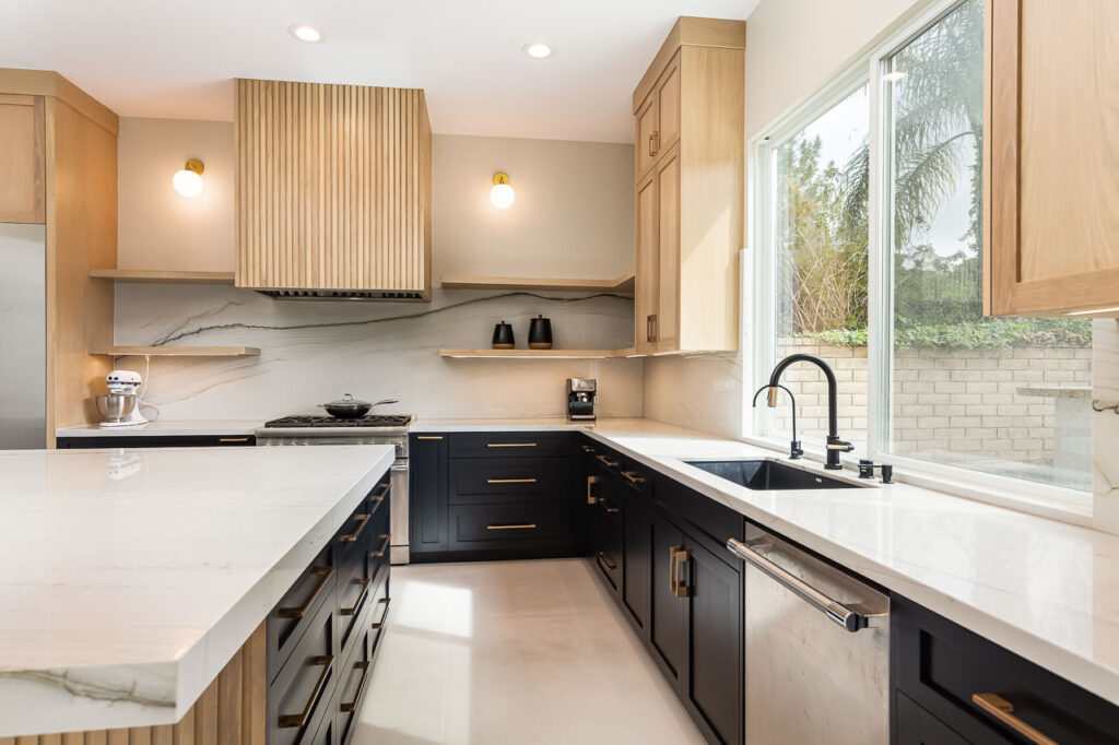 Modern San Diego kitchen remodel showcasing warm wood upper cabinetry and a fluted wood range hood that brings a sense of comfort and connection to nature. The design features custom cabinets with natural grain patterns accented by mixed metal hardware in matte black and gold.