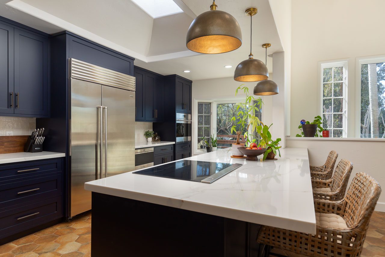 Induction cooktop island with quartz waterfall countertop and unlacquered brass dome pendants — Spanish Revival kitchen remodel Mission Hills San Diego 92103