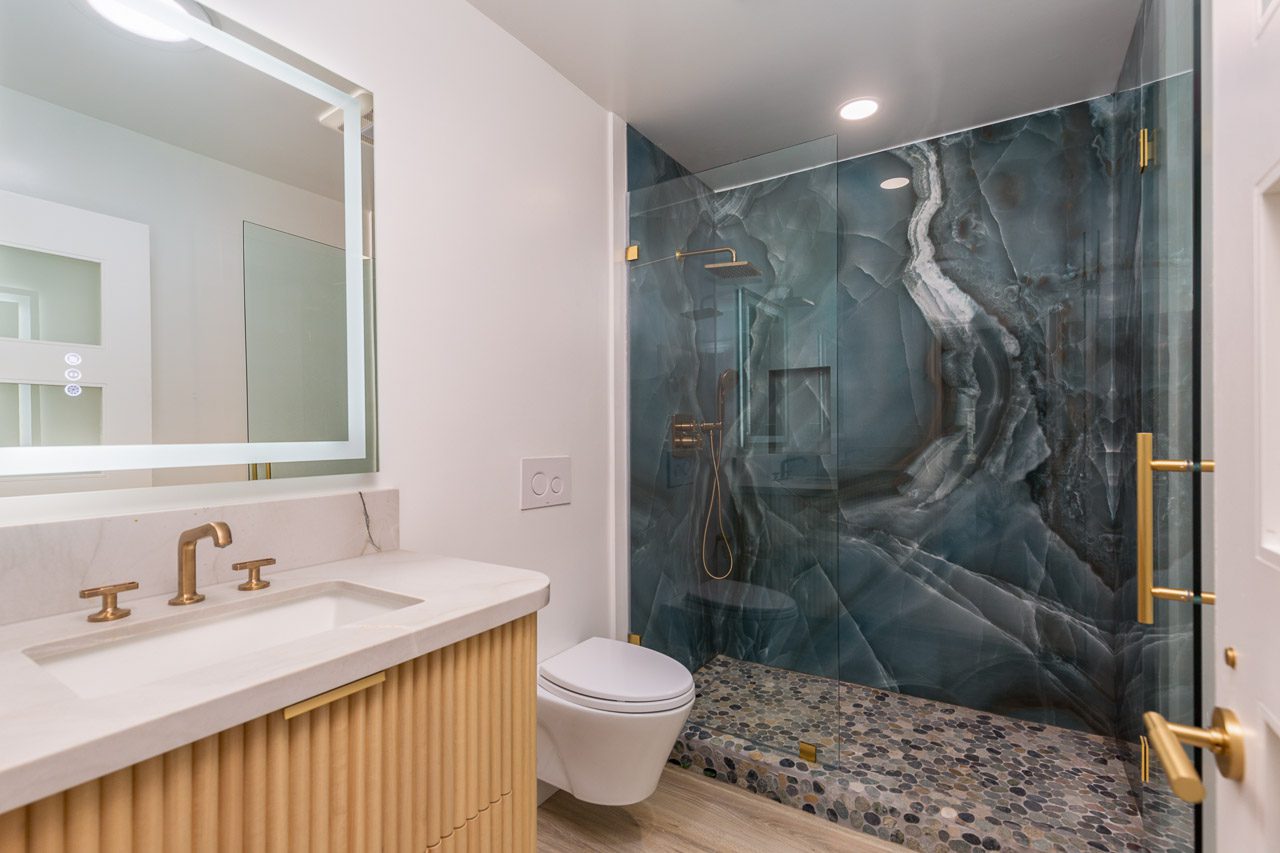 Luxury guest bathroom remodel San Diego 92118 — full blue onyx slab shower walls, fluted oak floating vanity, brushed gold fixtures