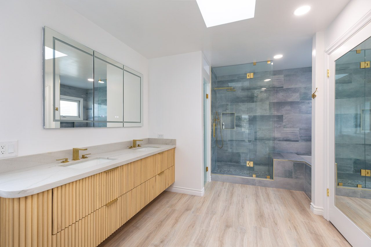 Master bathroom remodel San Diego waterfront 92118 — custom fluted oak vanity with brushed gold fixtures, triple LED-backlit medicine cabinet, layered lighting