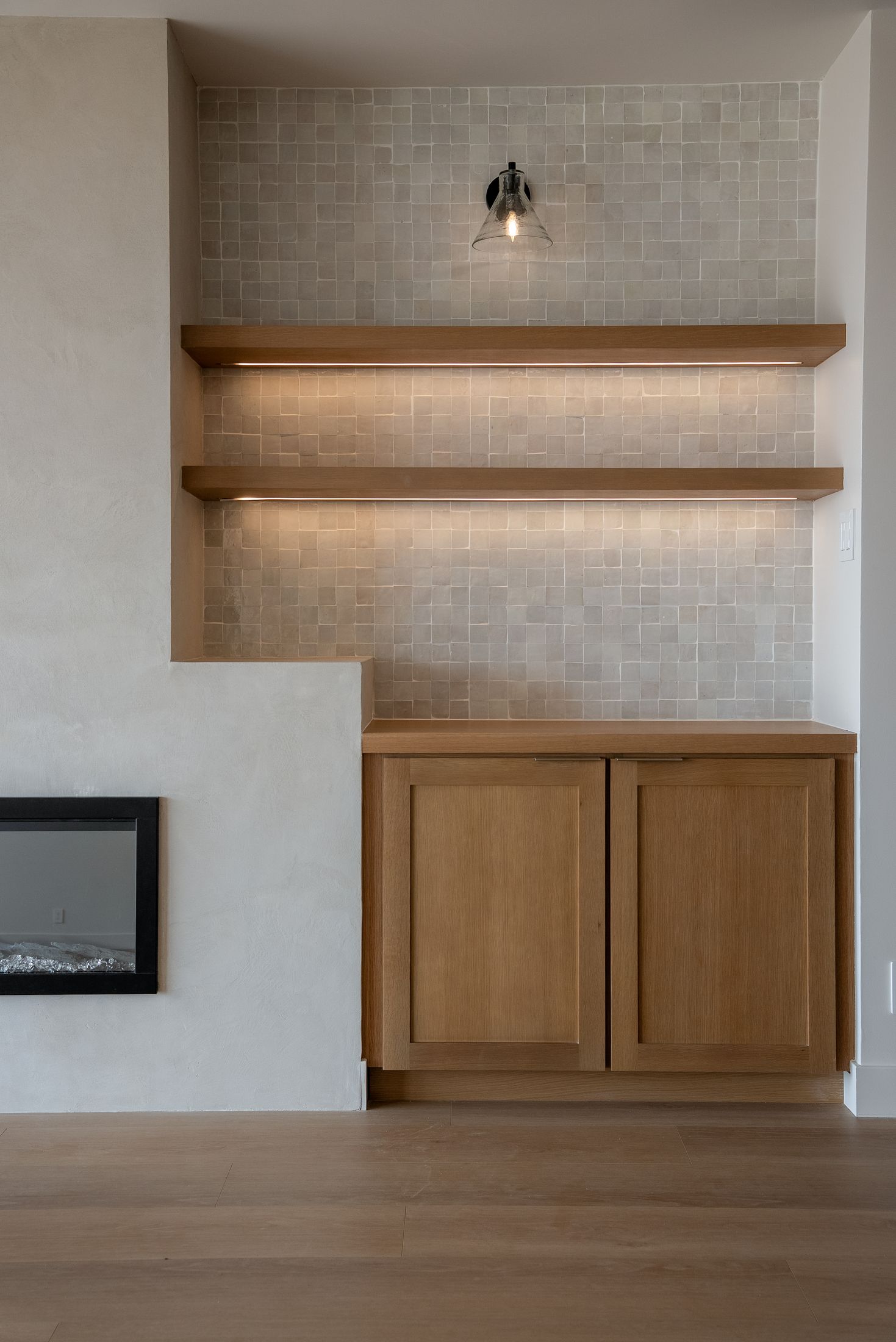 White oak floating shelves with LED strips over zellige tile beside a plaster fireplace, La Jolla living room