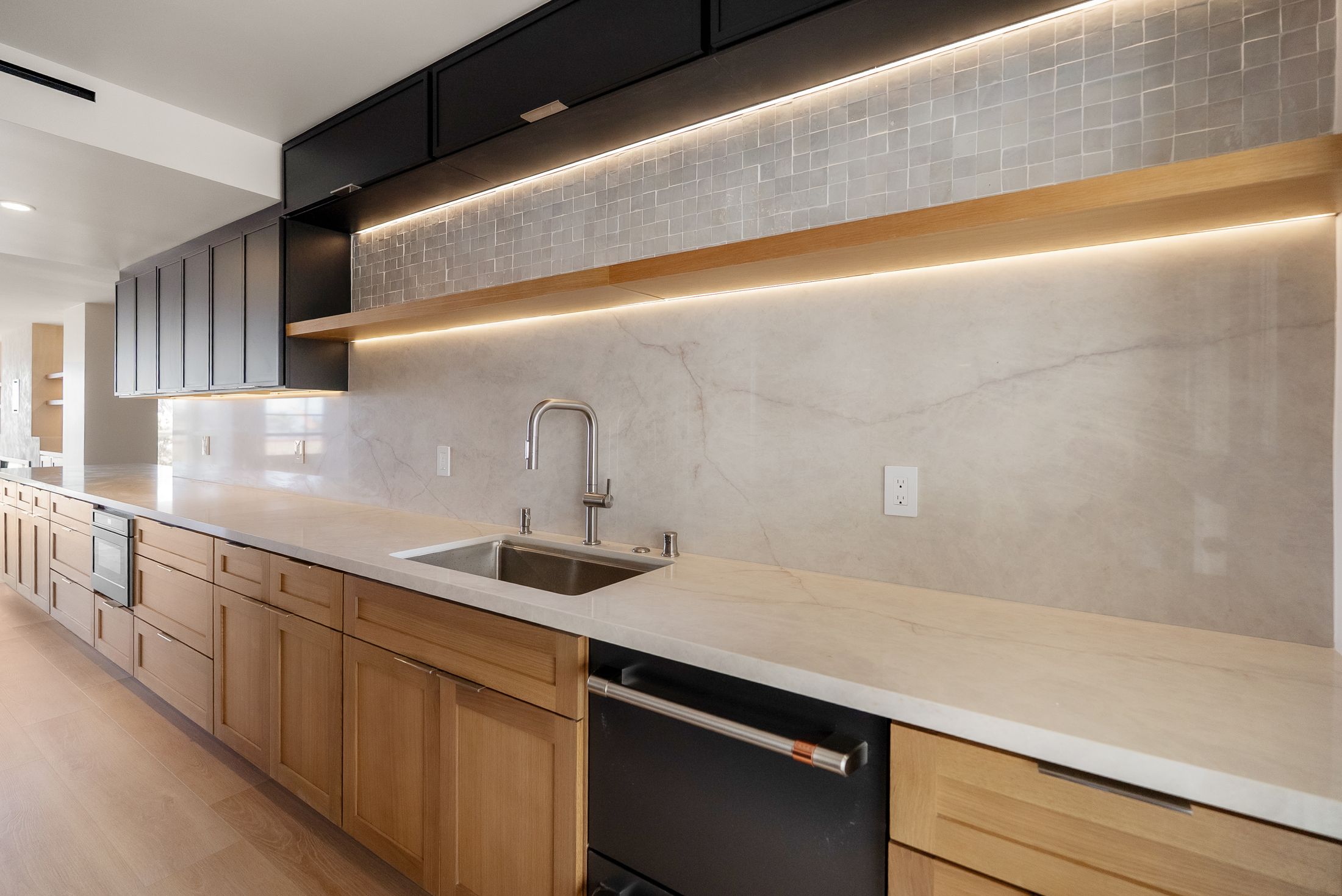 La Jolla galley kitchen with white oak lower cabinets, matte black uppers, full-height quartz backsplash and LED-lit floating shelf