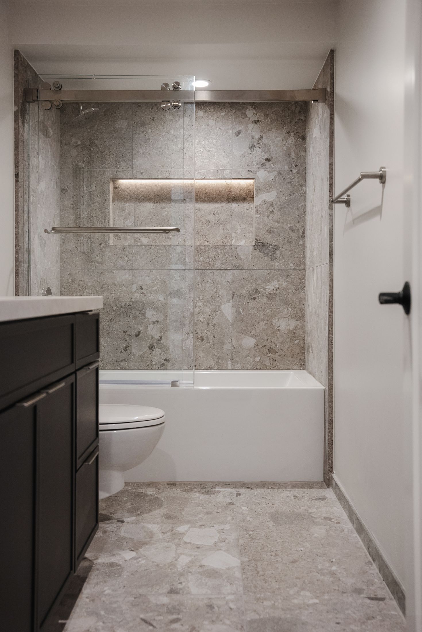Guest bathroom in La Jolla with terrazzo-look tile floor and walls, sliding glass tub enclosure and black vanity